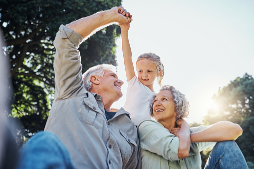 Grandparents playing together with a girl in the park in the morning. Family, love and grandchild bonding with grandmother and grandmother in a garden. Child holding hands with senior couple outside