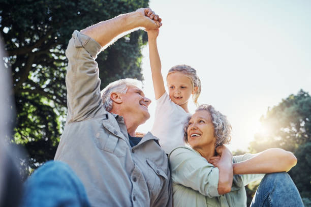 grandparents playing together with a girl in the park in the morning. family, love and grandchild bonding with grandmother and grandmother in a garden. child holding hands with senior couple outside - neto imagens e fotografias de stock