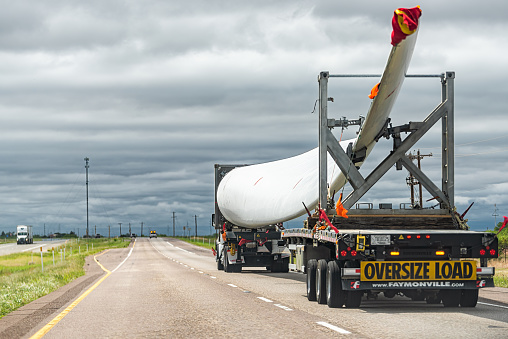 Amarillo, USA - June 1, 2022: Truck and trailer hauling transporting wind turbine blade with oversize load industrial yellow sign on highway road in Texas