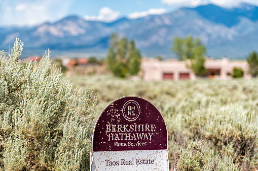 Taos, USA - June 19, 2019: Ranchos de Taos valley Sangre de Cristo mountains, Berkshire Hathaway realtor broker brokerage real estate sign by house