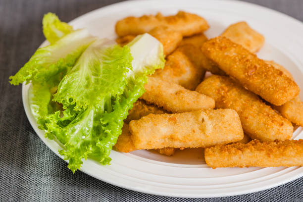 Deep-fried crunchy finger fish sticks served with green lettuce close-up on white plate on the table