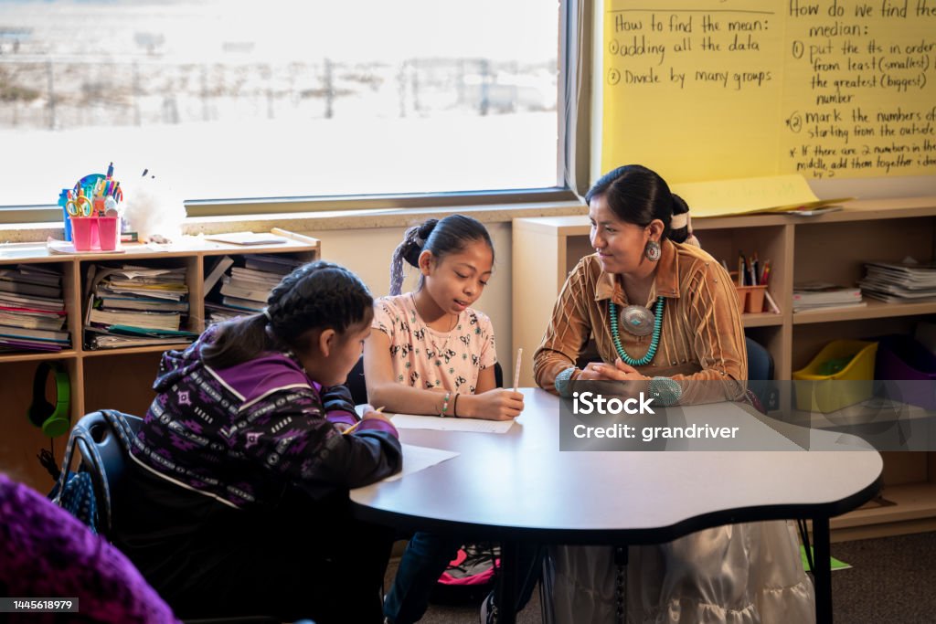 Young Female Teacher Assisting Elementary Age Students in Class Room at an Elementary School Young Female Indigenous Navajo Teacher Assisting Elementary Age Students in Class Room at an Elementary School in Monument Valley Utah Teacher Stock Photo
