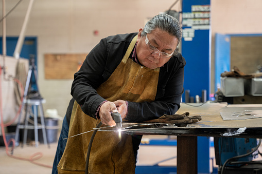 Indigenous Navajo Man in His Fifties Using a Welder or Cutting Torch on a Piece of Steel in a Metal Workshop in Monument Valley Utah