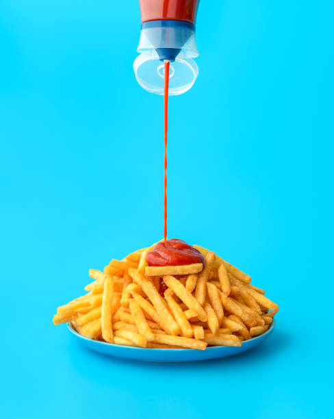 Pouring ketchup sauce over french fries, isolated on a blue background stock photo