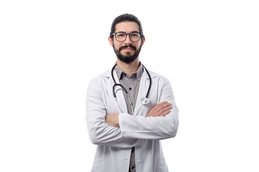 Young latin doctor with beard wearing white coat photographed in studio against white background.