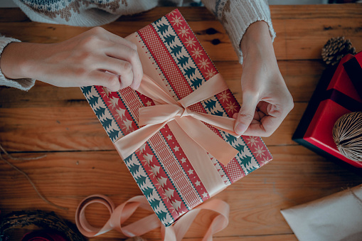 Woman hands wrapping xmas gifts into paper and tying them up with threads