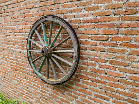Single wooden wheel of wagon hanging on the brick wall for decoration