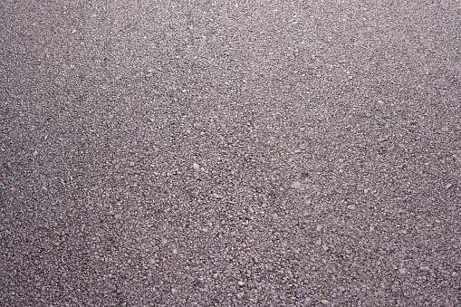 The image shows a road surface with black asphalt that has just been poured onto the road surface, Close up.