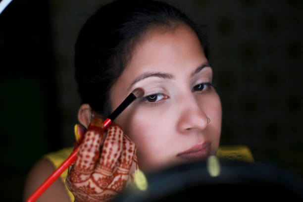 Close-up image of young Indian women self applying eyeshadow with brush in makeup studio.
