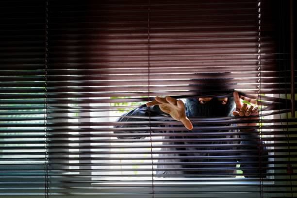 istock Thief in a black mask peeking through blinds 1445640968