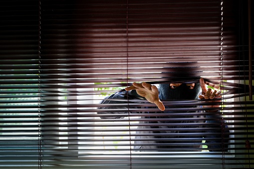 A thief in a black mask peeking through blinds