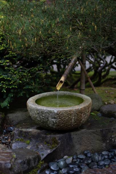 istock Vertical shot of a stone round pot with water that drips from a bamboo pipe into her 1445641437
