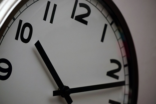 A closeup shot of a wall clock with a white base and black dials