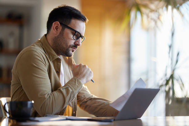 istock Young man working on paperwork and laptop at home office. 1445644471