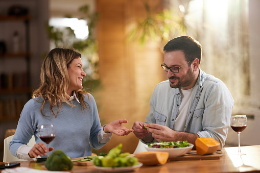 Happy couple communicating while preparing vegetables for healthy salad in dining room.