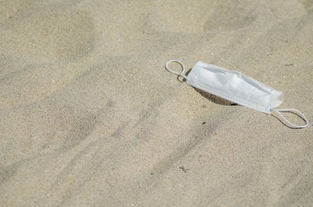 istock surgical mask lying on the beach, ecological concept 1445647747