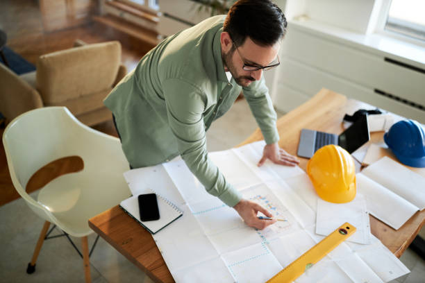 istock Above view of young building contractor analyzing plans while working at home office. 1445647757