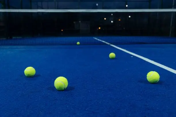 five balls on a blue paddle tennis court at dusk, racket sports