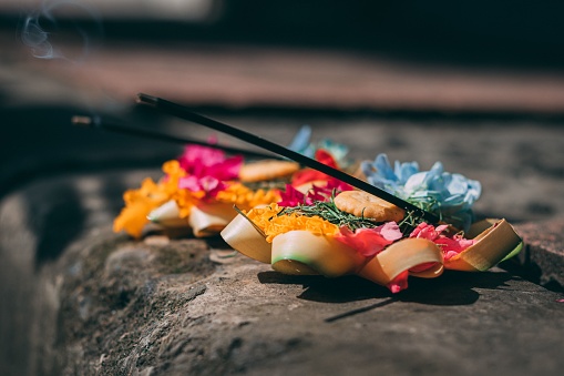 Hindu traditional oblation to gods and demons with flowers, food and aromatic sticks in the street in Bali island.