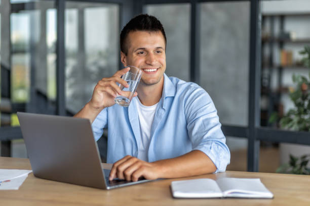 istock Successful happy man, office worker or entrepreneur, drinks fresh clean water, takes break after work sitting at the table in the office. Healthy lifestyle, recuperation concept 1445650457