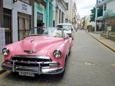La habanal, Cuba. 05/14/2018: American classic cars driving through the streets of la habana in cuba in which you can see its colonial architecture in contrast with the colorful vehicles.