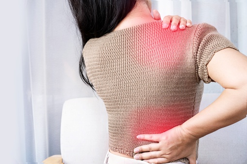 closeup woman suffering from shoulder pain or upper back spreading to the lower back