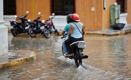 Campeche, Mexico – August 05, 2021: A motorcycle driving through deep water on the road after hurricane in Campeche, Mexico