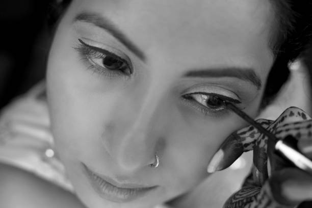 Young women of Indian ethnicity applying liquid eyeliner on eye lashes at home and she looking into mirror.