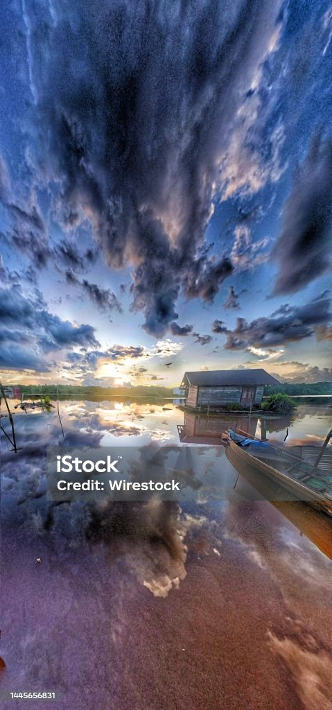 Vertical panoramic view of small house on the lakeshore against dark sunset clouds A vertical panoramic view of small house on the lakeshore against dark sunset clouds Blue Stock Photo