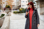 Smiling young woman texting on mobile phone while walking in the city