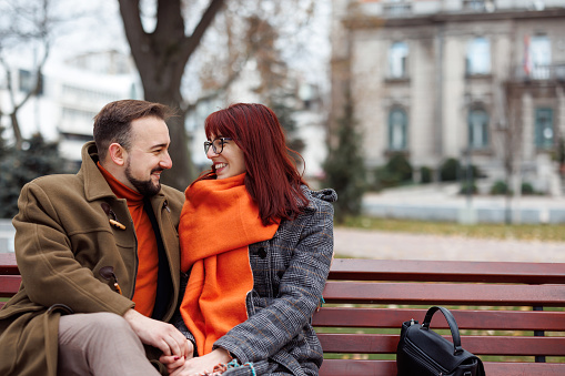 Young couple in love sitting on bench in the city, holding hands and smiling