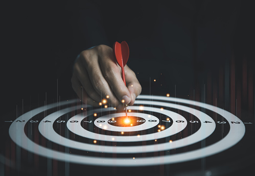 Businessman holding red dart aiming at center of target board and digital technology graph