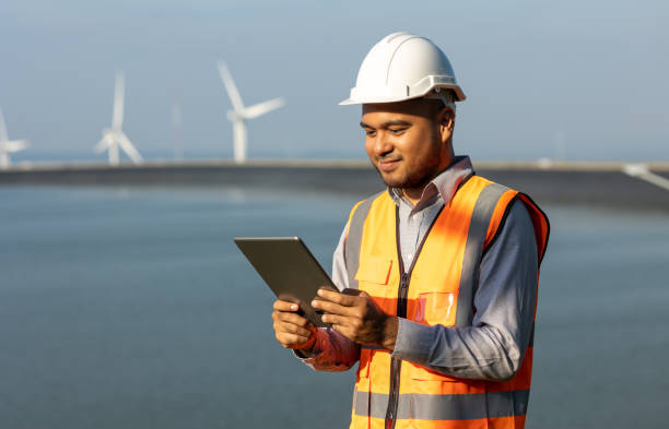 istock Engineer India man working with tablet at windmill farm hydroelectric Generating electricity clean energy. Wind turbine farm and water power generator by green energy. Engineer control electric power 1445672743