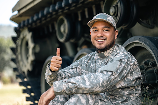 Asian man special forces soldier against on the field Mission. Commander Army soldier military defender of the nation in uniform sitting near battle tank while state of war.