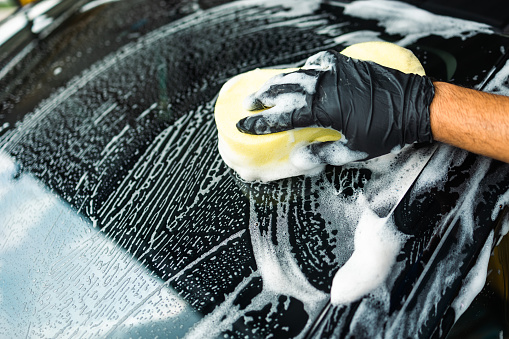 Man worker washing car service with foam and sponge. Car wash cleaning wipe station. Employees clean a vehicle professionally.