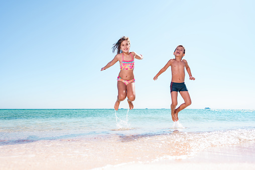 Joyful children having fun while jumping in summer day on the beach. Copy space.