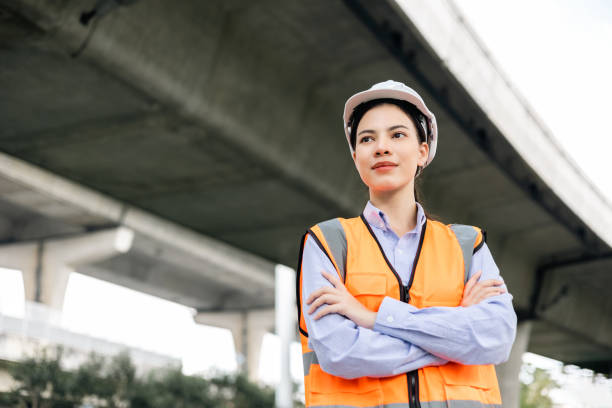 istock Asian engineer worker woman or architect looking construction with white safety helmet in construction site. Standing at highway concrete road site. Progress planning of highway bridge. 1445674372