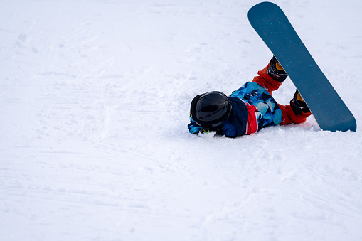 Person with snowboard on the snow. One Asian child is falling on the ground. Winter sport with copy space.