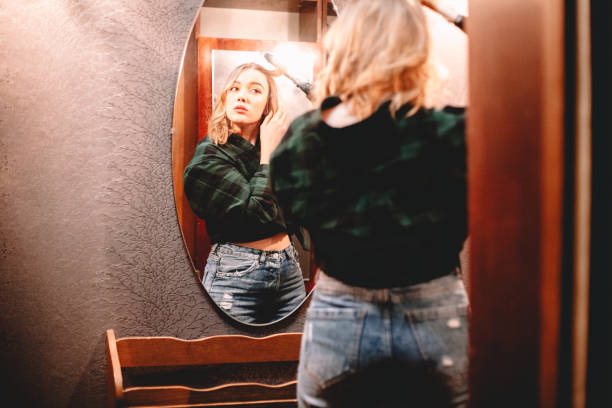istock Young woman using curling iron looking at herself in the mirror at home getting ready to go out 1445688637