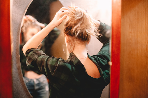 Young woman tying hair while looking at herself in the mirror at home getting ready to go out