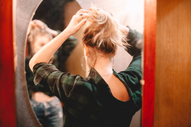 Young woman tying hair while looking at herself in the mirror at home getting ready to go out stock photo