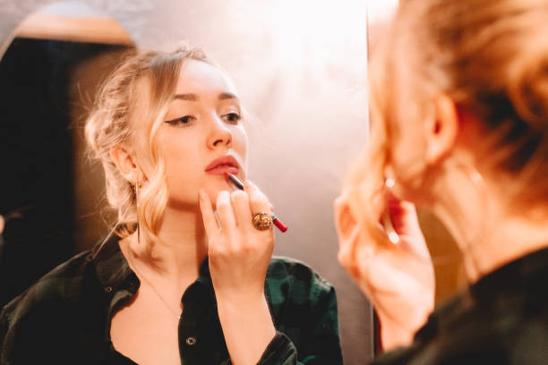 Young woman using lip pencil while drawing contours applying lipstick doing make up at home getting ready to go out