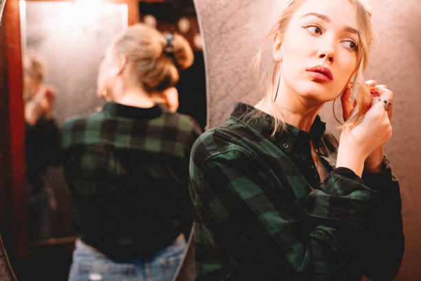 istock Young woman putting on hoop earring while standing in front of mirror at home getting ready to go out 1445688679