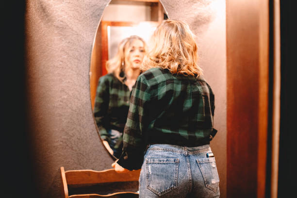 istock Young woman looking at herself in the mirror while standing in hallway at home getting ready before going out 1445688692