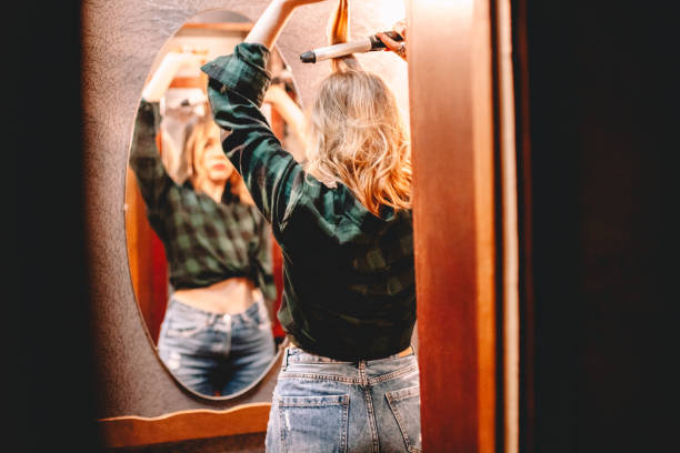 istock Young woman using curling iron looking in the mirror at home getting ready to go out 1445688728