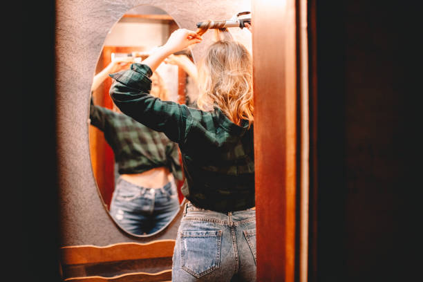 istock Young woman using curling iron looking in the mirror at home preparing to go out 1445688780