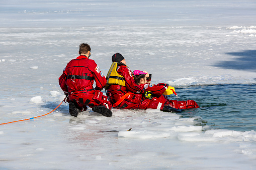 Krakow, Poland - February 20, 2021: Water rescue exercises in winter on a frozen lake in a hole, lifeguards dressed in red suits with specialized equipment