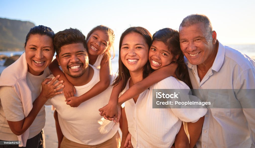Portrait of happy family with children smile and hug together on a sunset beach. Adorable little kids bonding with mother, father, grandmother and grandfather outdoor on summer vacation at the ocean Family Stock Photo