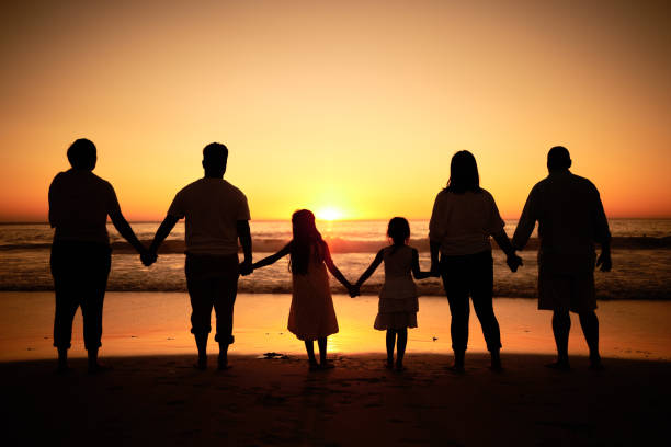 grande silhouette familiale sur la plage avec les vagues de la mer, le coucher de soleil à l’horizon et se tenir la main pour le bien-être du développement, le soutien et l’amour. les enfants et le groupe de personnes regardent l’océan sur une ma - senior adult outdoors wellbeing sky photos et images de collection