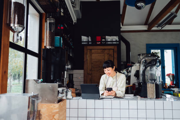 istock Happy Female Employee Using Mobile Phone And Digital Tablet While Working In A Coffee Shop 1445692628